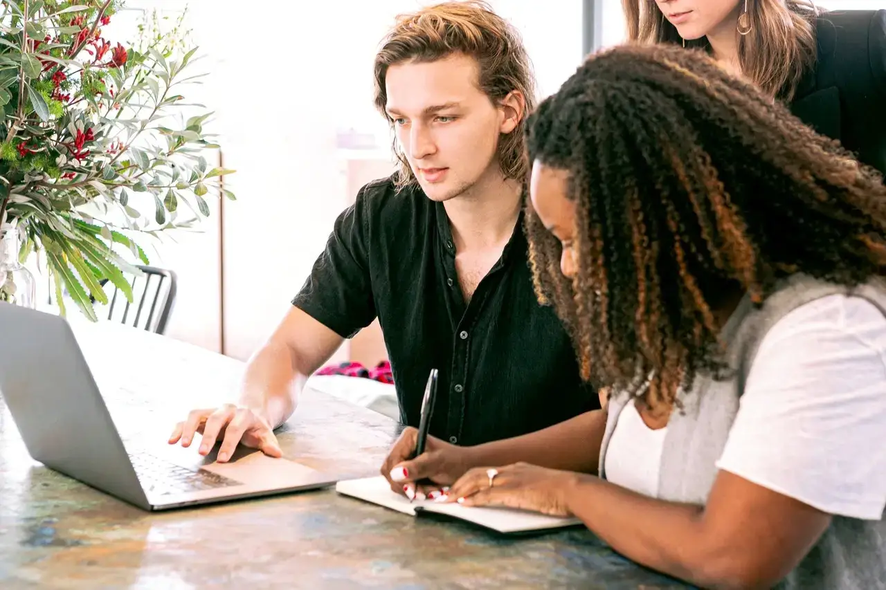 A diverse team of professionals in a modern office collaborating around a laptop, showcasing the benefits of hiring a marketing consultant