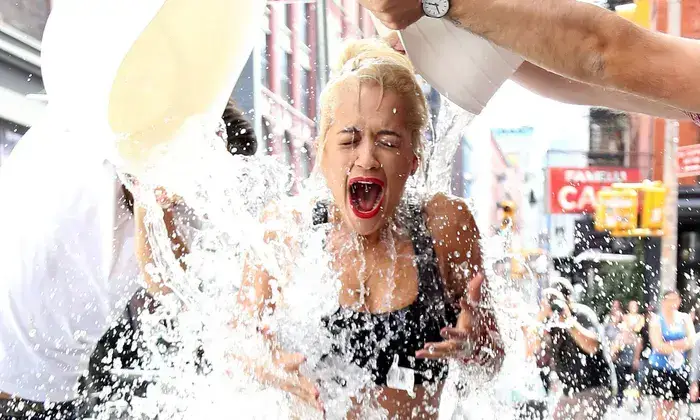 a woman getting drenched with water as part of a social media trend, similar to the "ice bucket challenge". this image represents the bandwagon effect, where people are more likely to participate in an activity if they see others doing it. this phenomenon is commonly observed in social media trends that quickly gain popularity and become viral.