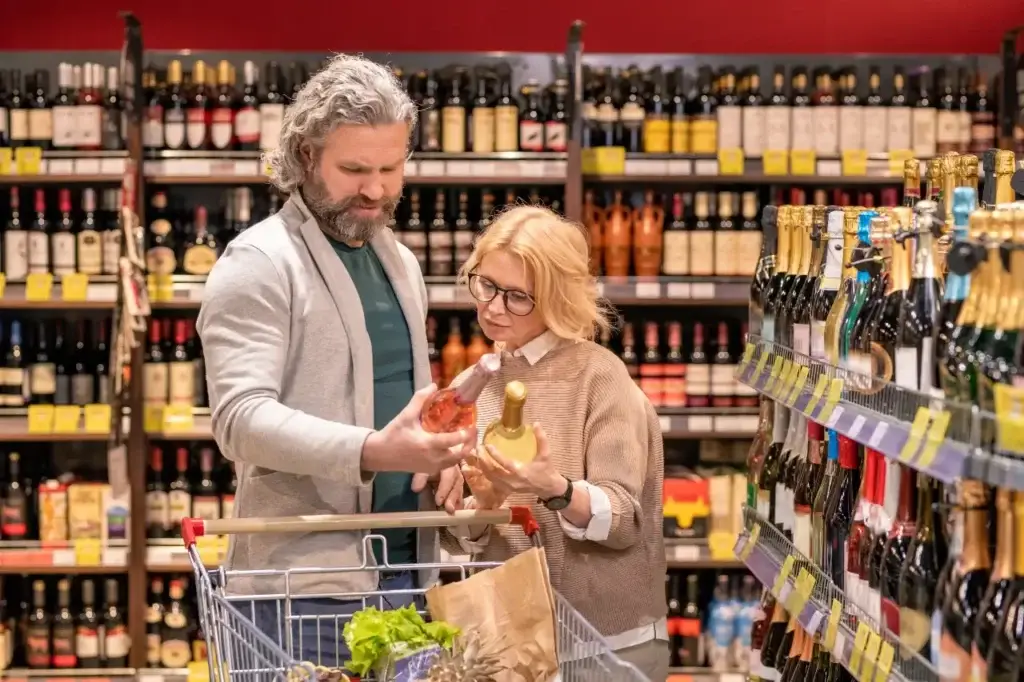 A couple in a grocery store scrutinizing wine bottles, representing the blemishing effect in everyday shopping decisions.