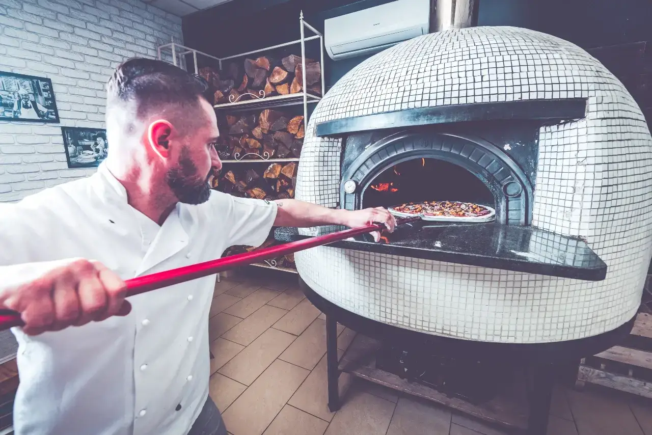 Chef sliding a pizza into a traditional oven, illustrating hands-on SEM for local businesses in the food industry.